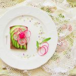 A beautifully plated radish and avocado tartine on a vintage tray with lace accents.