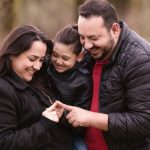 A joyful family of three enjoys a tender moment outdoors, depicting warmth and love.