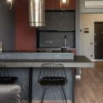 Dining zone furnished with counter and chairs in modern apartment with island style kitchen equipped with range hood and illuminated by hanging lamps
